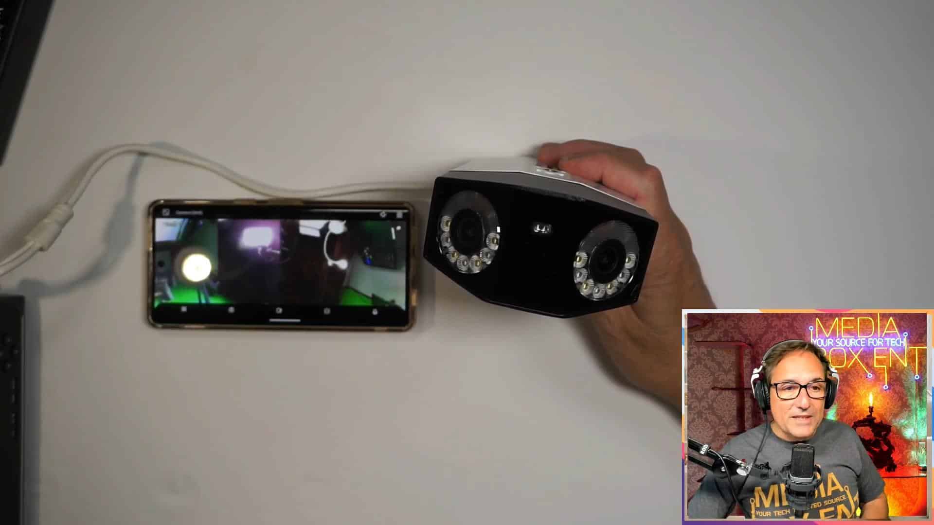Technology reviewer holds a REOLINK 4K PoE security camera in hand with its live feed visible on a smartphone, illustrating the camera’s functionality and connectivity.