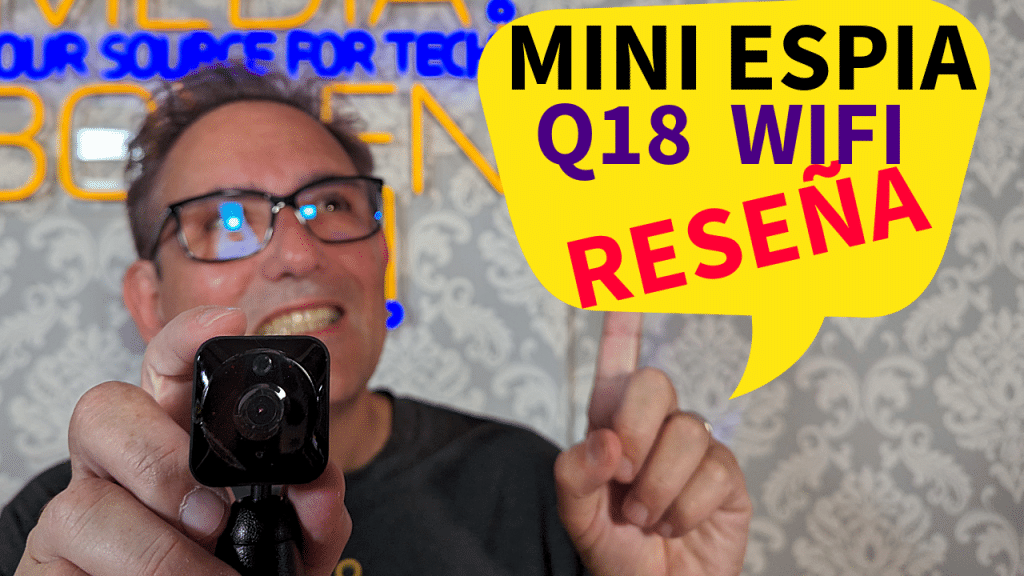 Hombre sosteniendo una mini cámara espía Q18 WiFi mientras sonríe y señala un globo de texto amarillo que dice "MINI ESPIA Q18 WIFI RESEÑA